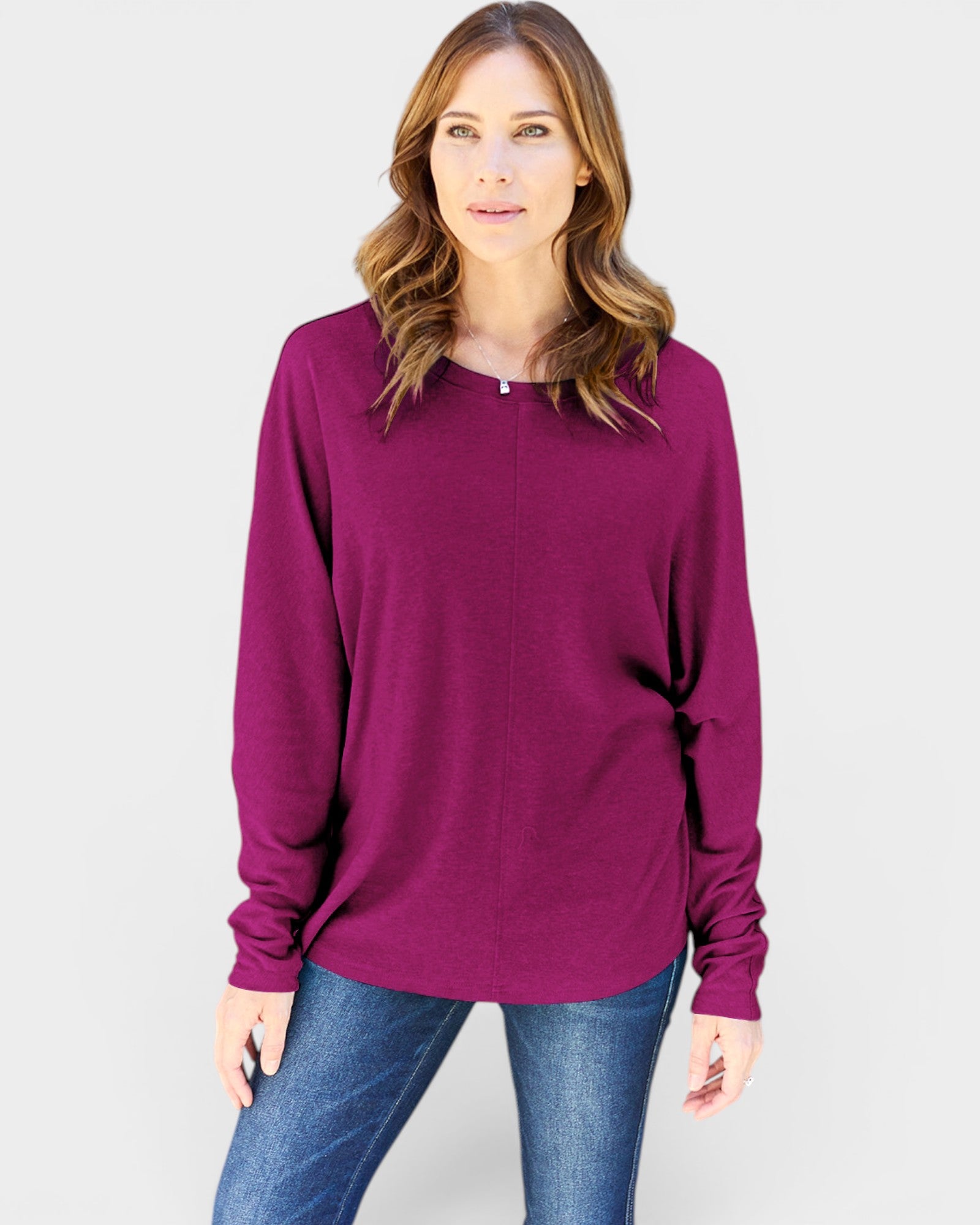 Woman wearing a purple long-sleeve top and blue jeans on a light gray background