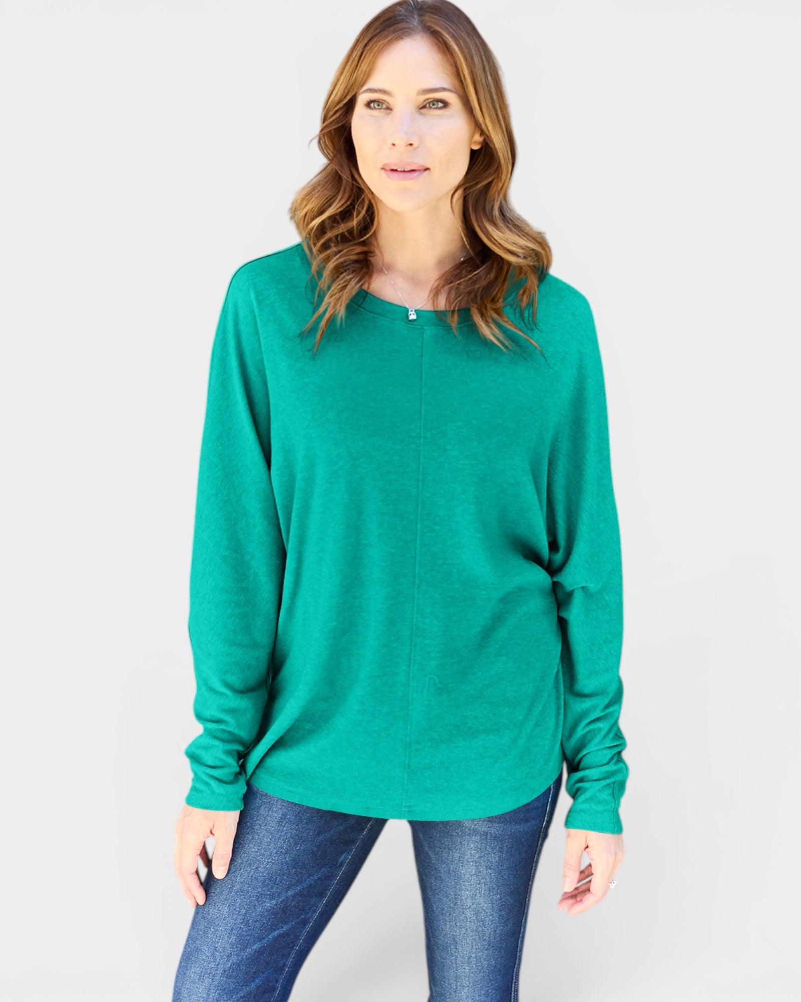 Woman wearing a green sweater and blue jeans on a light gray background