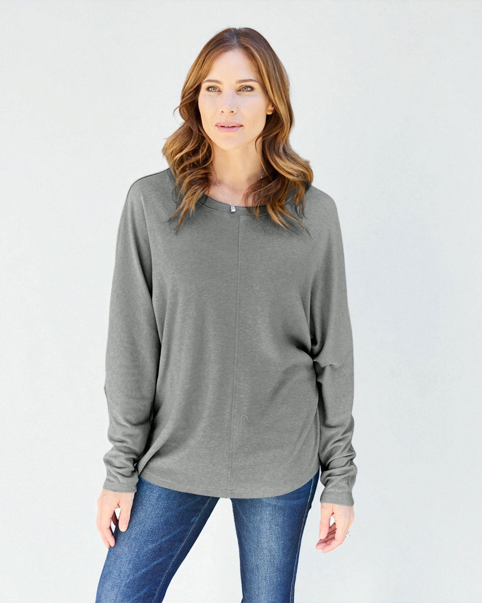 Woman wearing a gray long-sleeve top and blue jeans on a white background