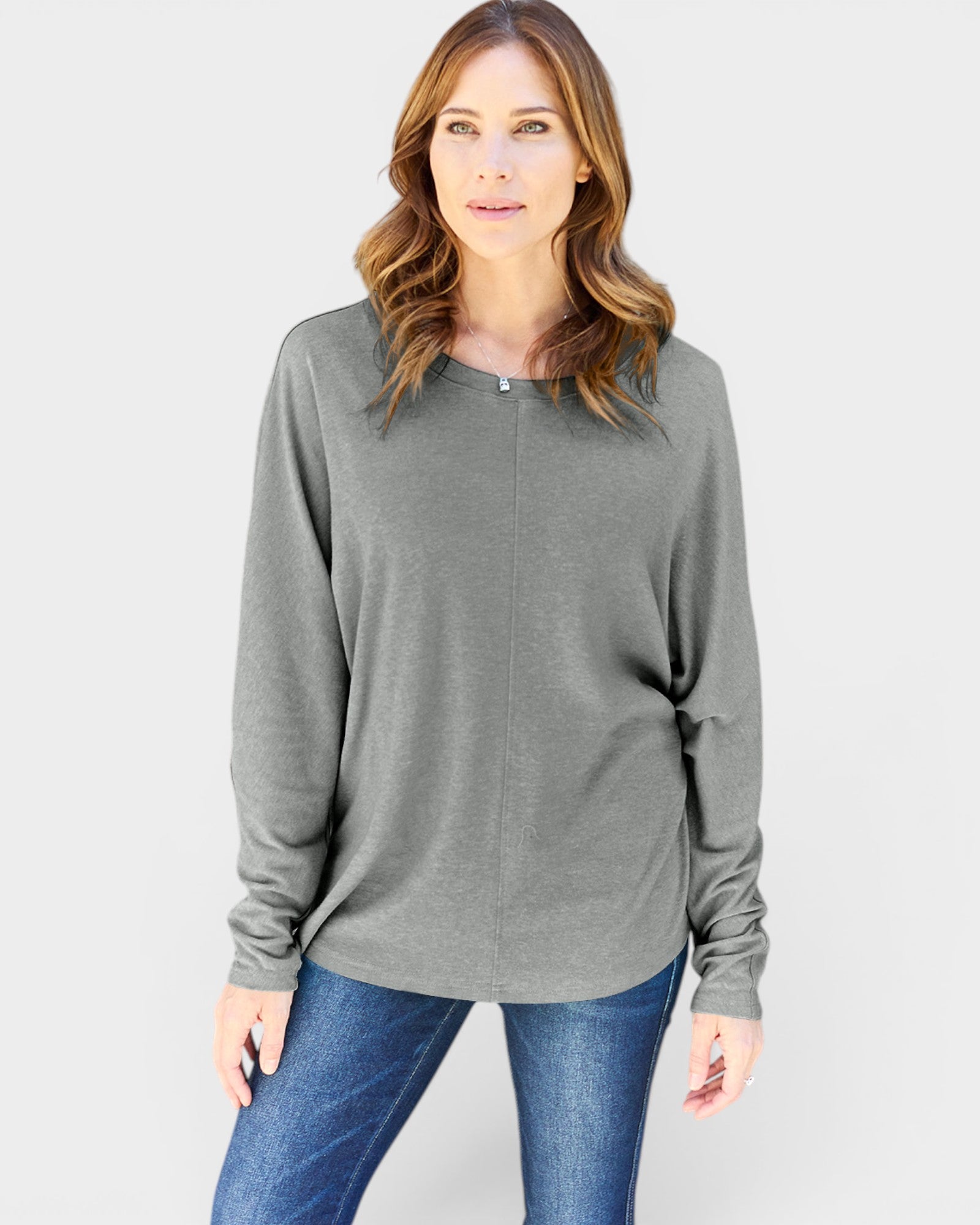 Woman wearing a gray long-sleeve top and blue jeans on a white background