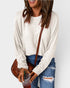 Person wearing a white long-sleeve top and blue jeans, holding a brown bag and a drink.