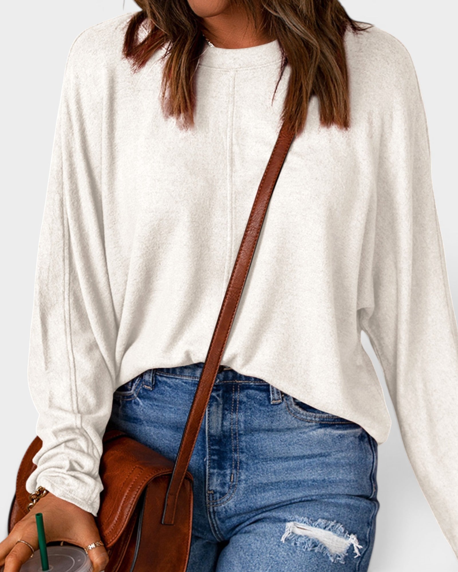 Person wearing a white sweater and blue jeans with a brown shoulder bag on a light gray background