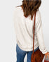 Person wearing a white sweater and blue jeans with a brown leather bag on a light gray background