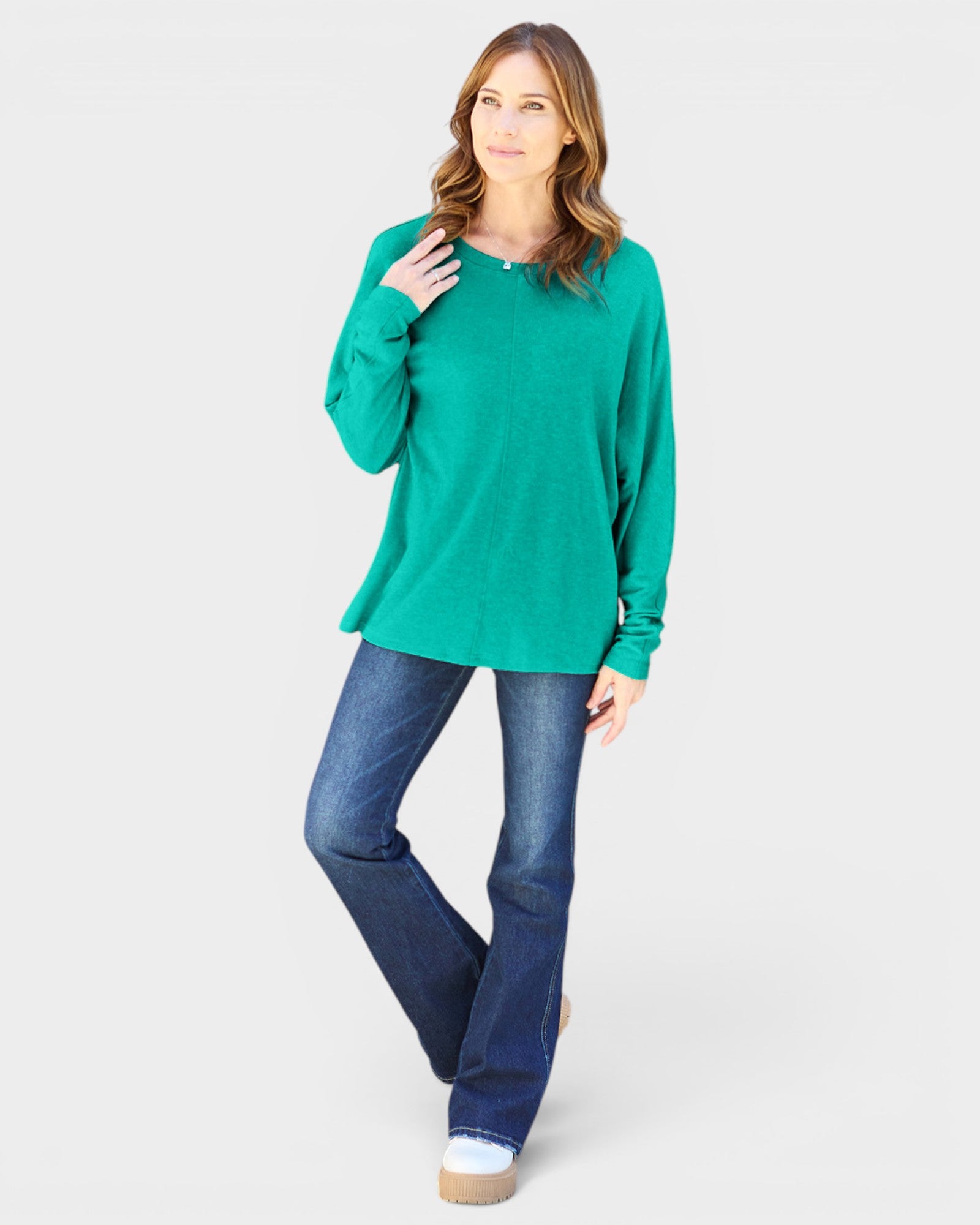 Woman wearing a green sweater and blue jeans on a white background