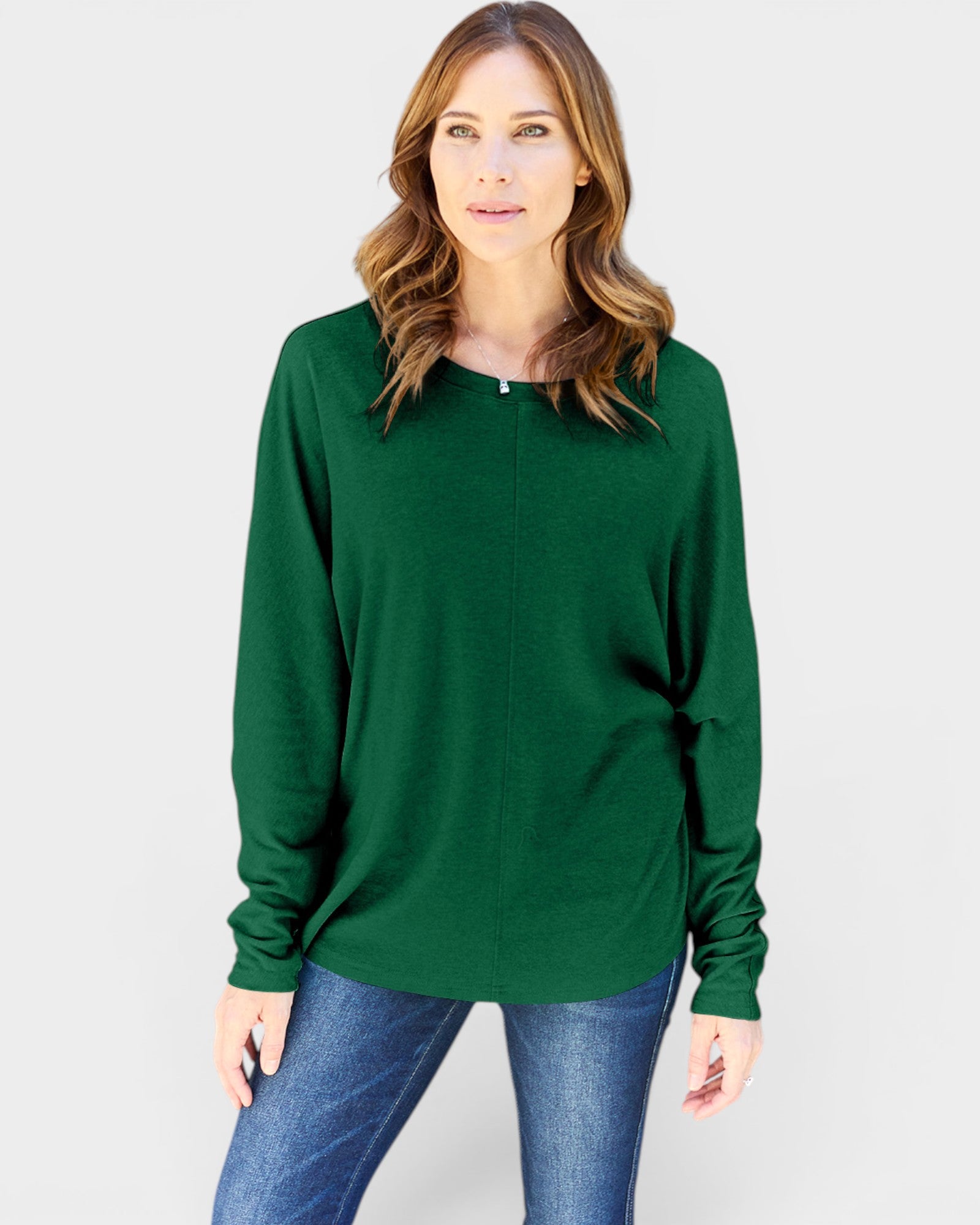 Woman wearing a green long-sleeve top and blue jeans on a light gray background