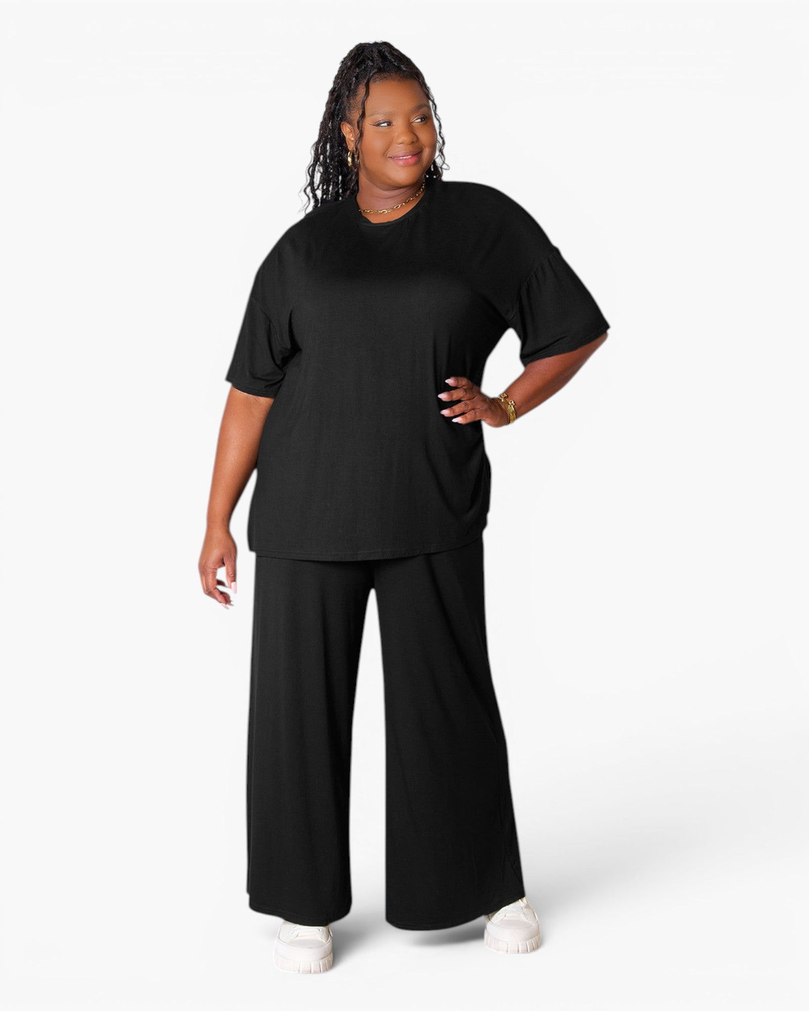 A woman modeling a black short-sleeve t-shirt and matching black wide-leg pants against a clean white studio background.