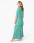 A woman modeling a teal green two-piece lounge set consisting of a short-sleeve draped top and matching wide-leg pants, shown from a side-back angle against a plain white studio background.