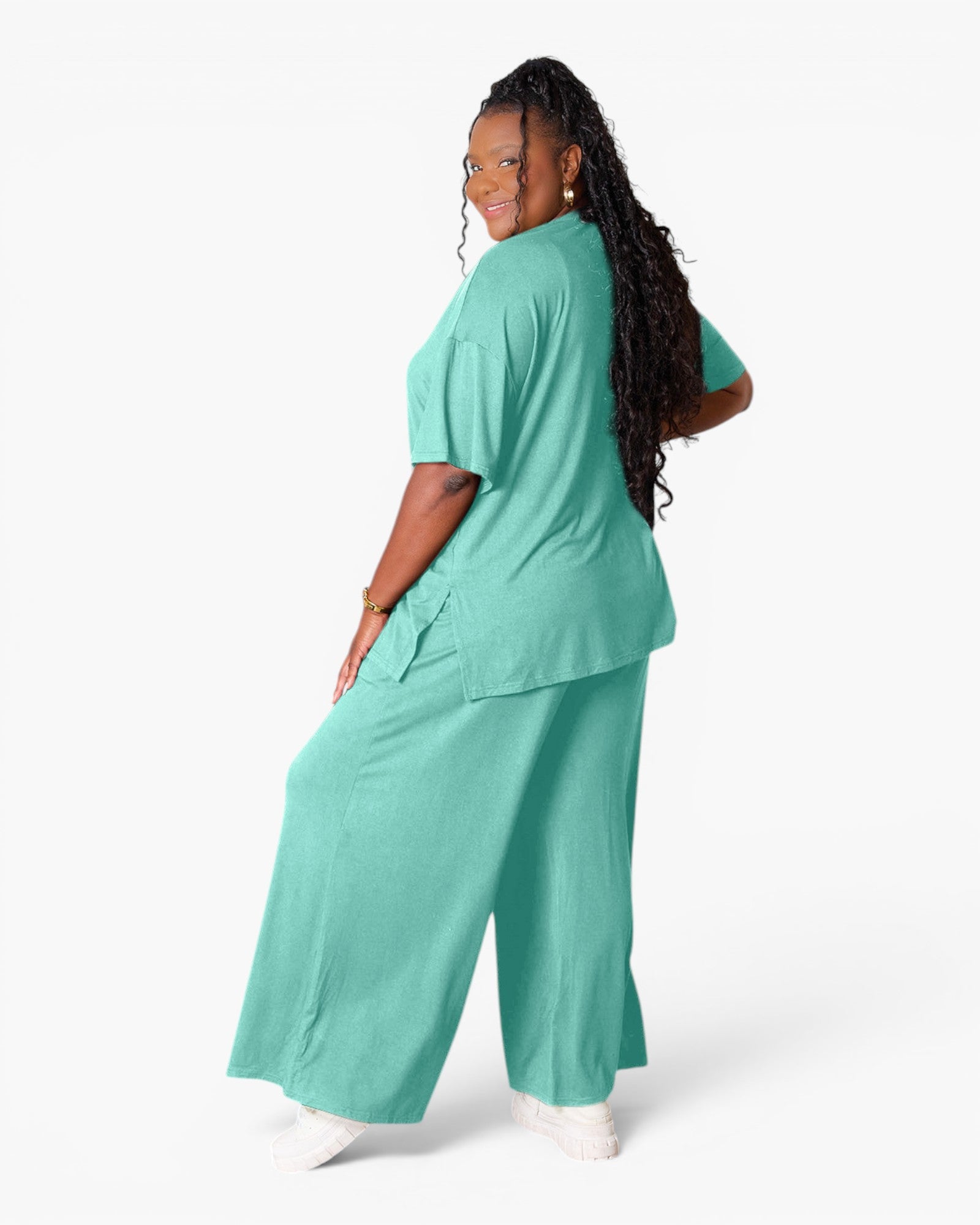 A woman modeling a matching two-piece scrub set in mint green, featuring a short-sleeve top and wide-leg pants, shown from a three-quarters back view against a plain white studio background.