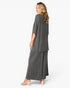 A woman modeling a dark gray two-piece outfit consisting of a short-sleeve draped tunic top and matching wide-leg pants, shown from a side-back angle against a light gray studio background.