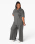 A woman modeling a matching two-piece lounge set in dark gray, featuring a short-sleeve henley-style top and wide-leg pants, against a plain white studio background.