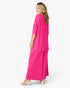 A woman modeling a bright pink two-piece outfit consisting of a short-sleeve draped top and matching wide-leg pants, shown from a side-back angle against a plain white studio background.
