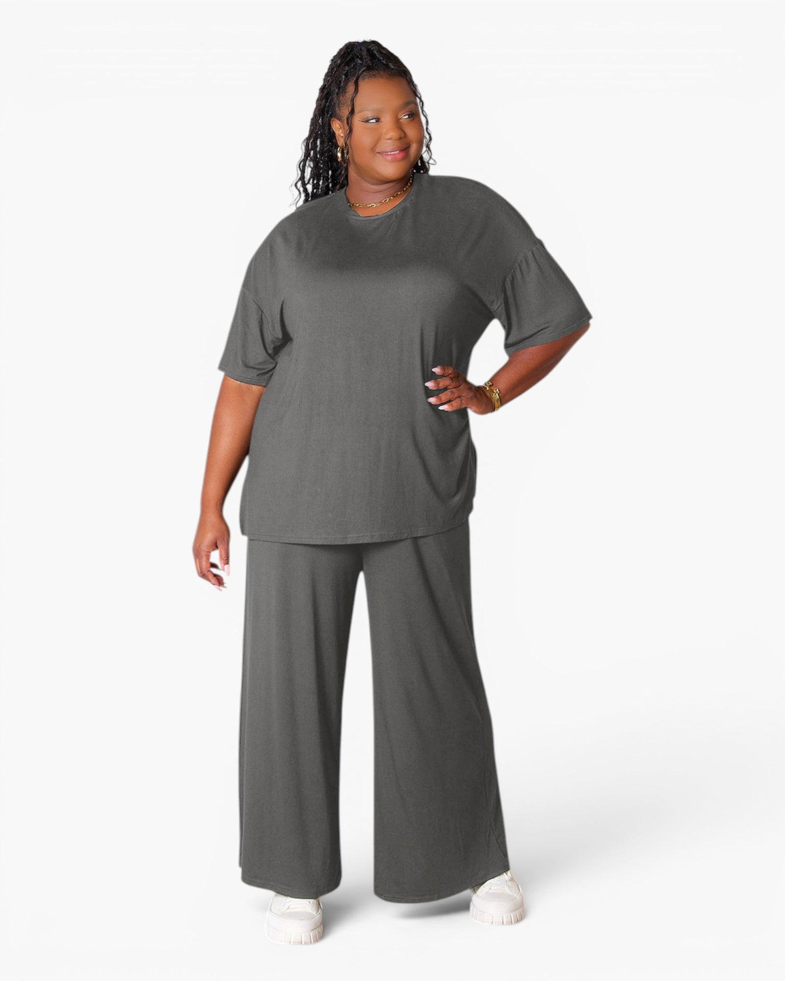 A woman modeling a dark gray two-piece lounge set consisting of a short-sleeve crewneck t-shirt and matching wide-leg pants, photographed against a clean white studio background.