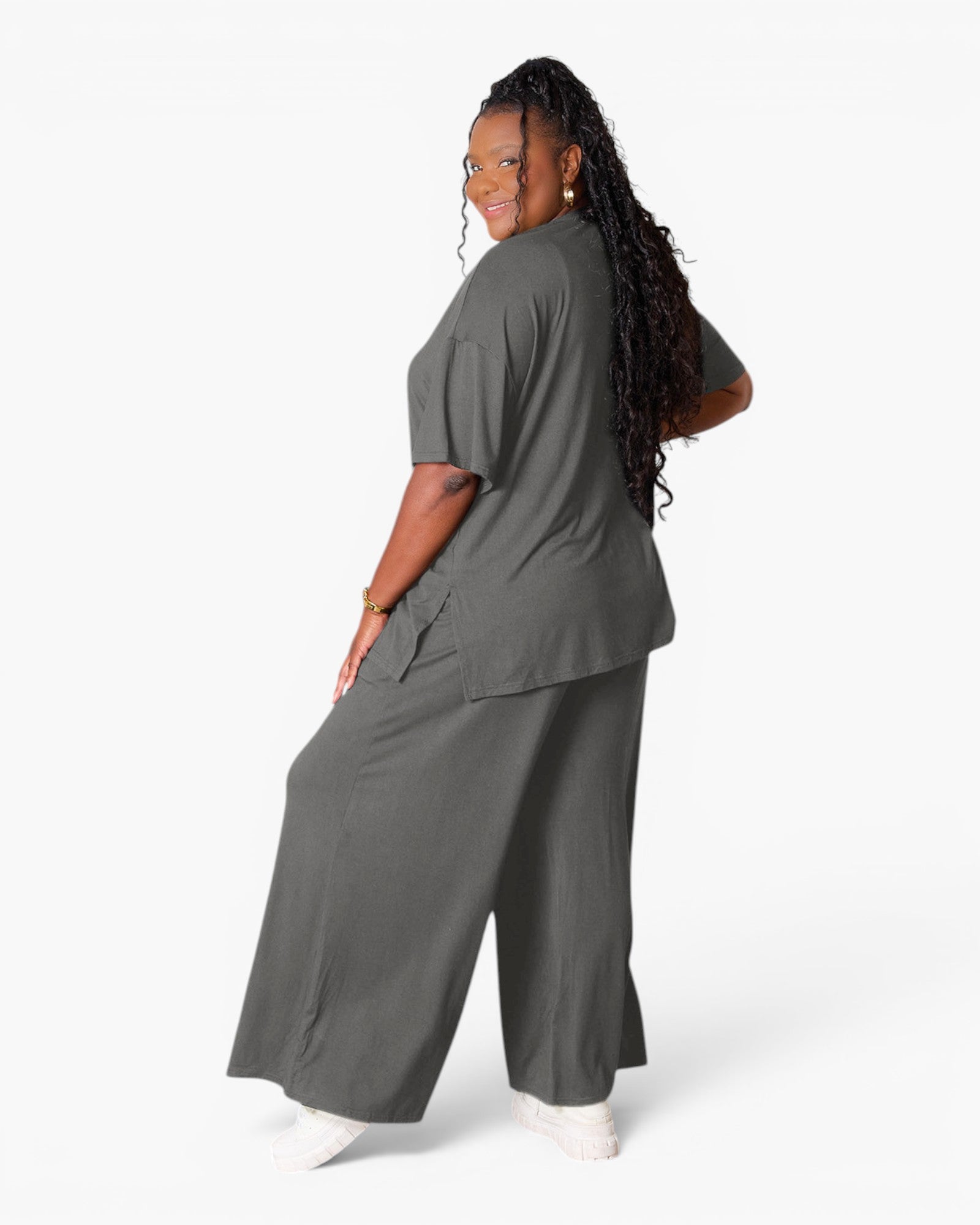 A woman modeling a dark gray two-piece scrub set consisting of a short-sleeve top and matching wide-leg pants, shown from a three-quarters back view against a plain white studio background.