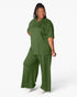 A woman modeling a matching two-piece lounge set in olive green, featuring a short-sleeve V-neck top and wide-leg pants, against a plain white studio background.
