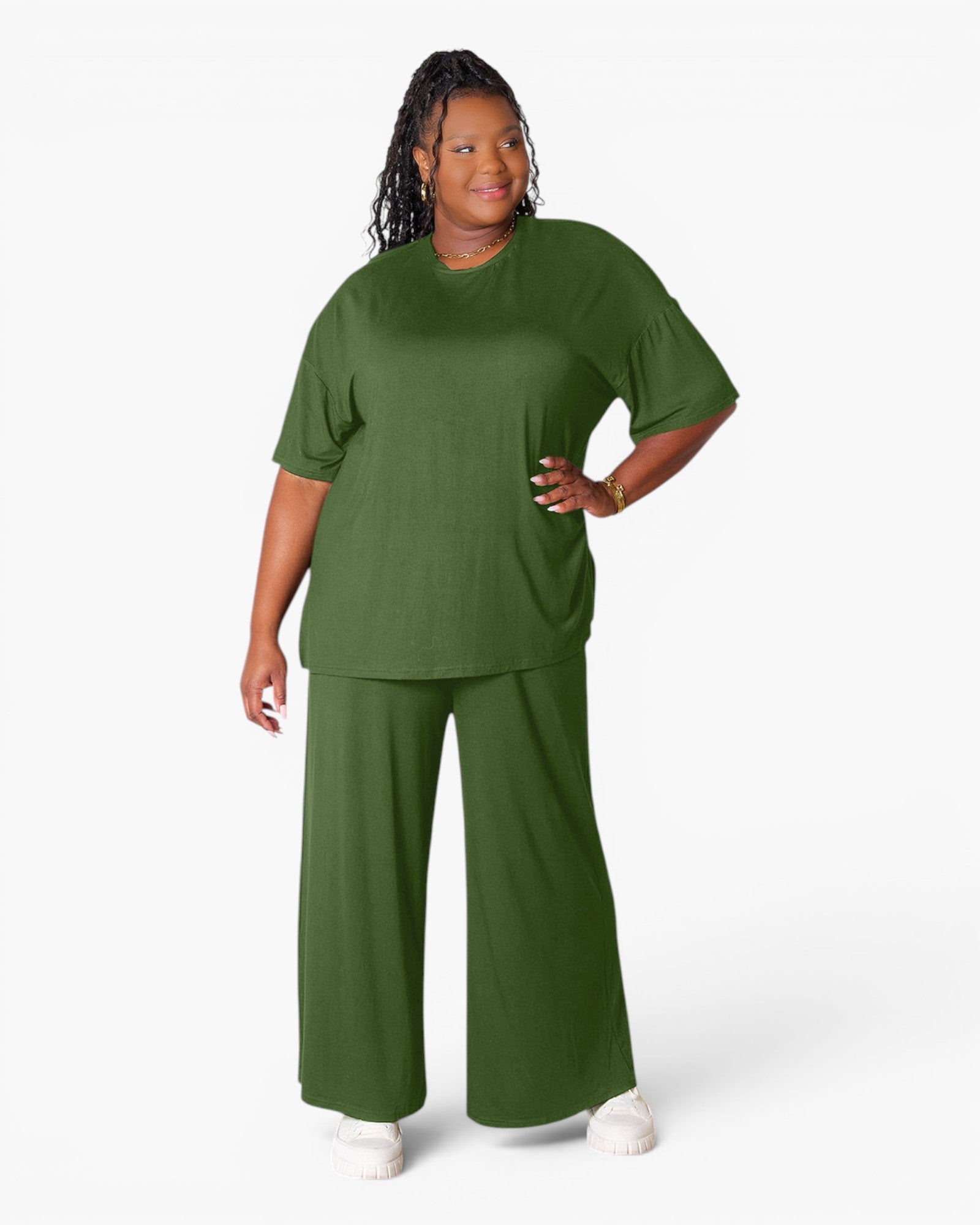 A woman modeling a matching olive green lounge set consisting of a short-sleeve crewneck top and wide-leg pants, paired with white sneakers against a plain white studio background.