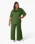 A woman modeling a matching olive green lounge set consisting of a short-sleeve crewneck top and wide-leg pants, paired with white sneakers against a plain white studio background.