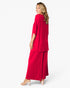 A woman modeling a bright red two-piece outfit consisting of a draped long-sleeve top and matching wide-leg pants, shown from a side-back angle against a plain white studio background.
