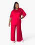 A woman modeling a bright red two-piece lounge set consisting of a short-sleeve crewneck top and matching wide-leg pants, photographed against a clean white studio background.