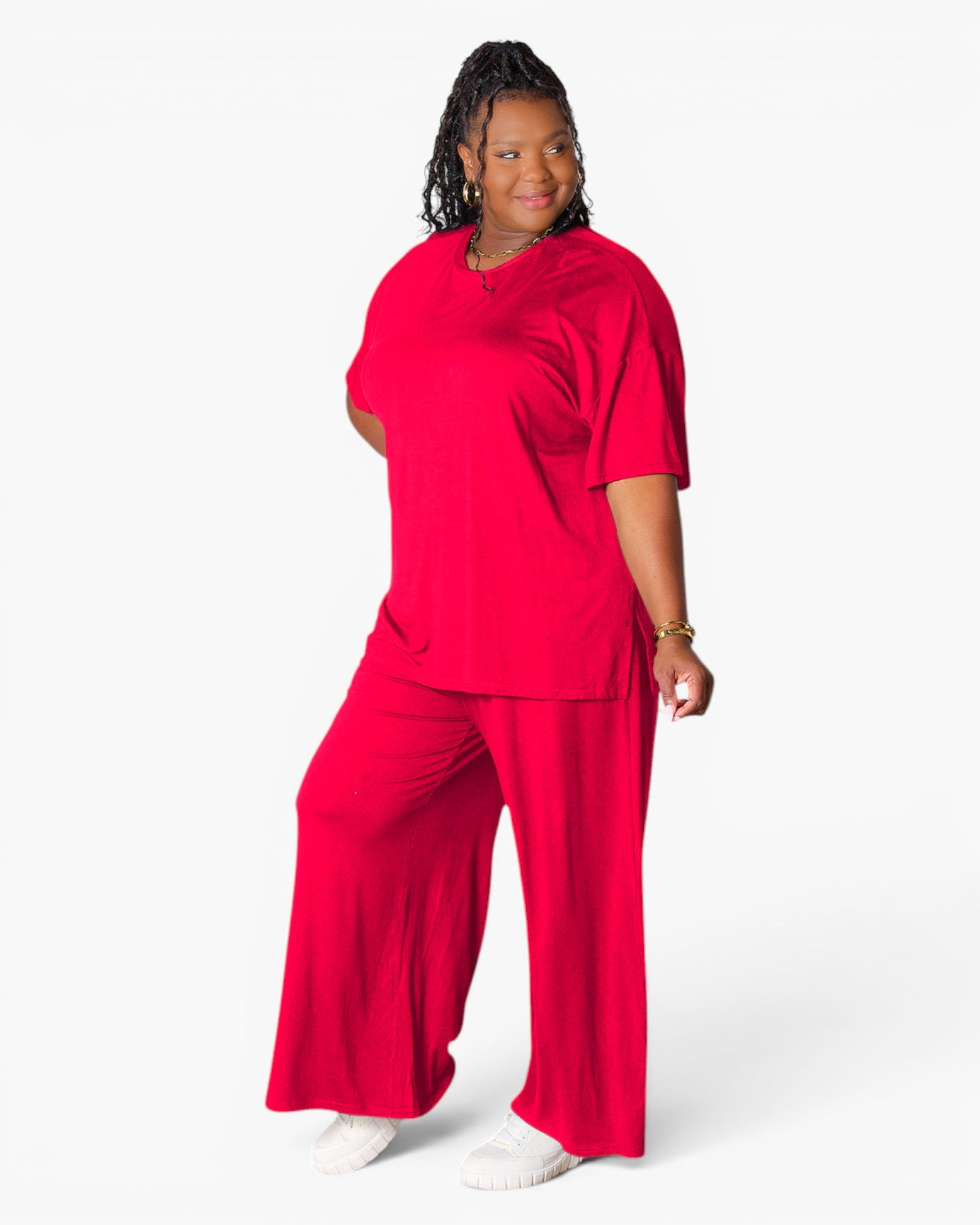A woman modeling a bright red two-piece loungewear set consisting of a short-sleeve V-neck top and matching wide-leg pants, photographed against a clean white studio background.