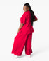 A woman modeling a bright red two-piece lounge set consisting of a short-sleeve top and matching wide-leg pants, shown from a three-quarters back view against a plain white studio background.