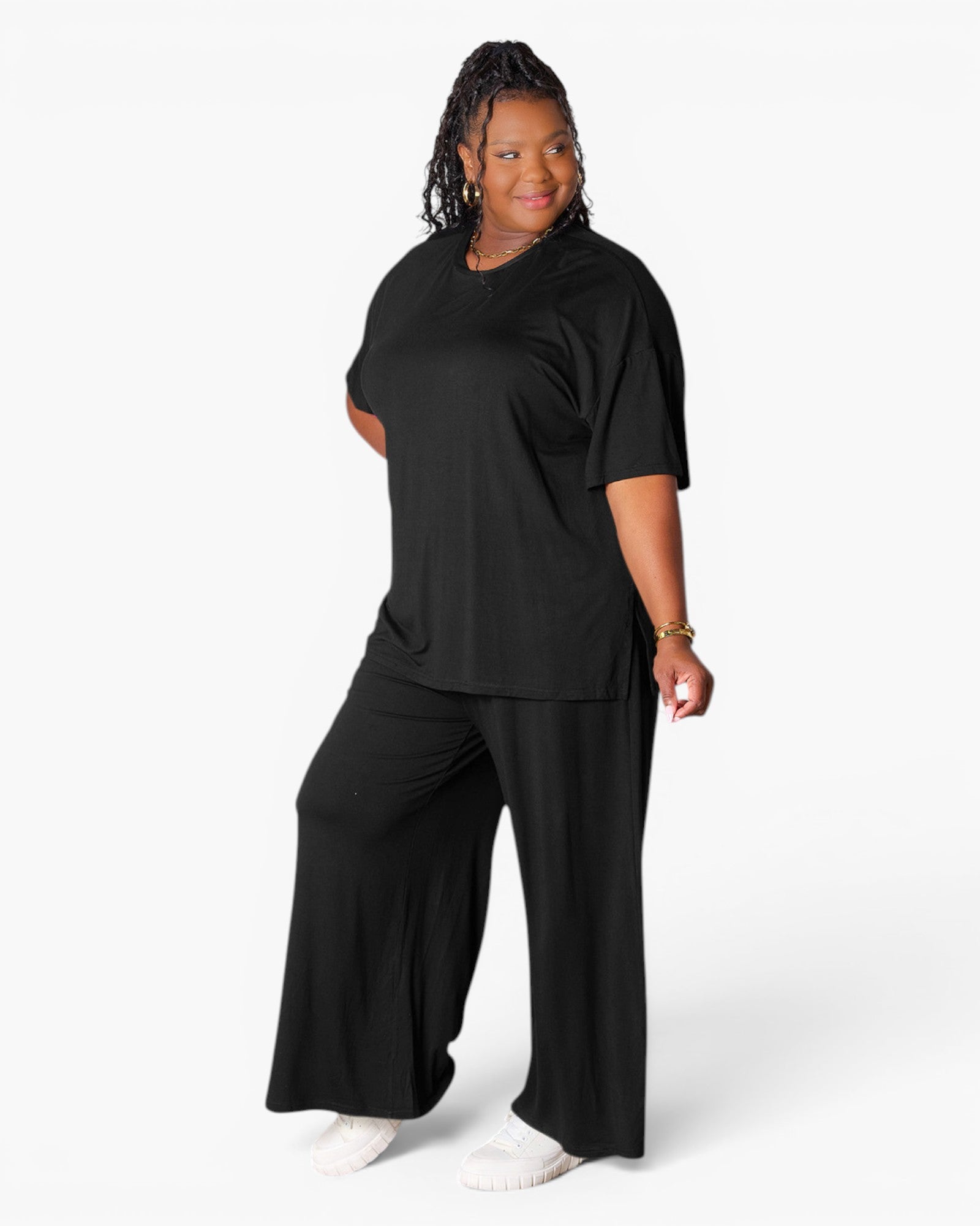 A woman modeling a black short-sleeve V-neck top and matching black wide-leg pants against a light gray studio background.