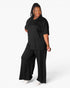 A woman modeling a black short-sleeve V-neck top and matching black wide-leg pants against a light gray studio background.