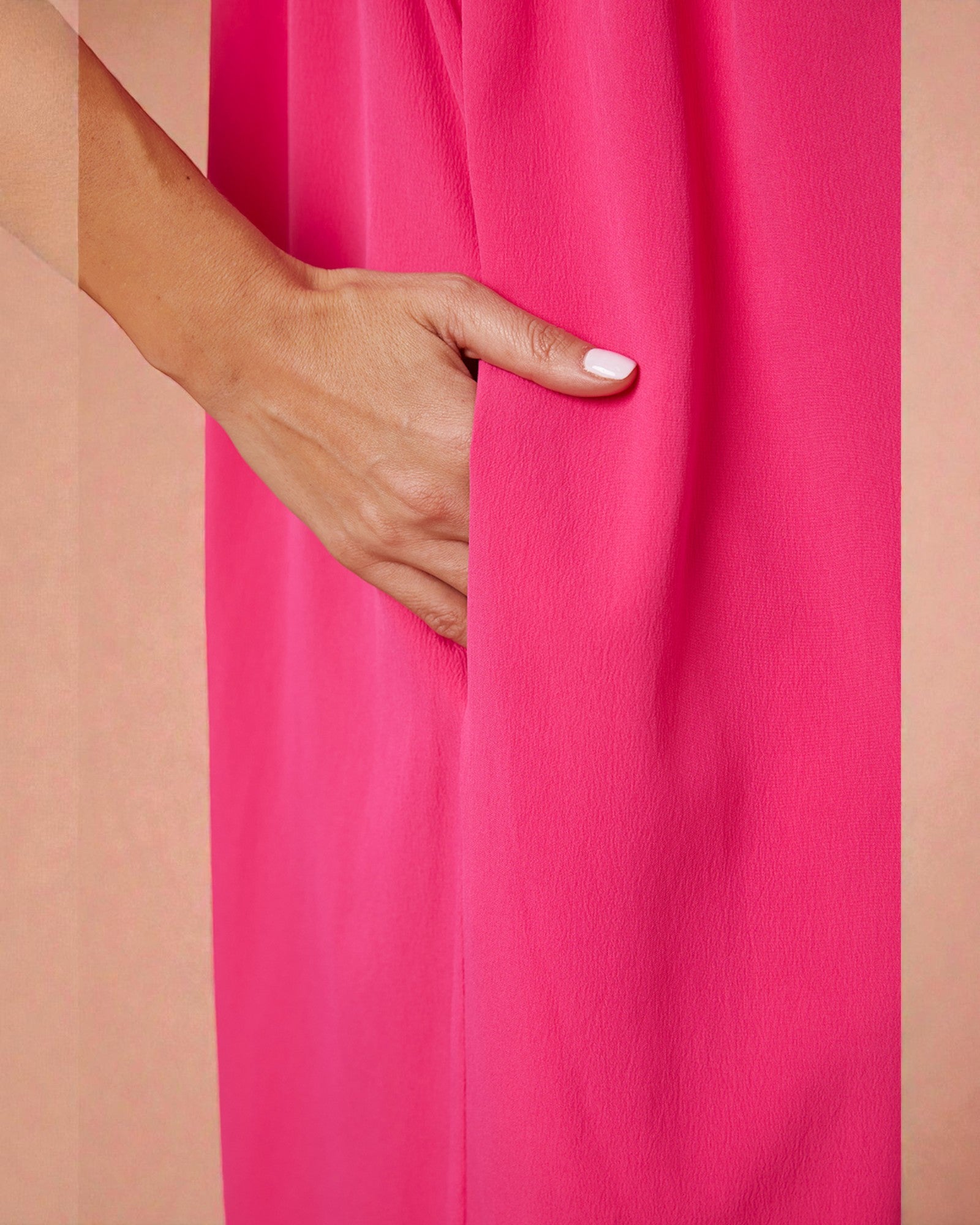 Hand with white nail polish on a bright pink fabric background