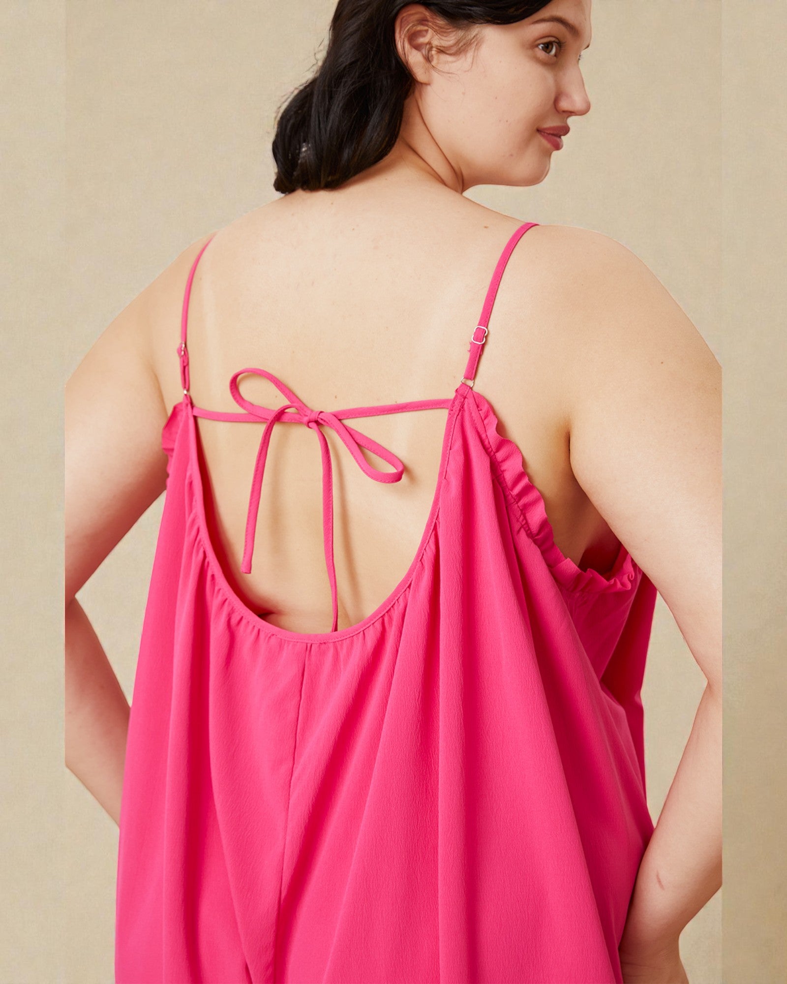 Woman wearing a pink dress with thin straps and tied back on a beige background