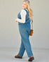 Woman wearing a blue jumpsuit with a white shirt underneath, standing against a plain background.