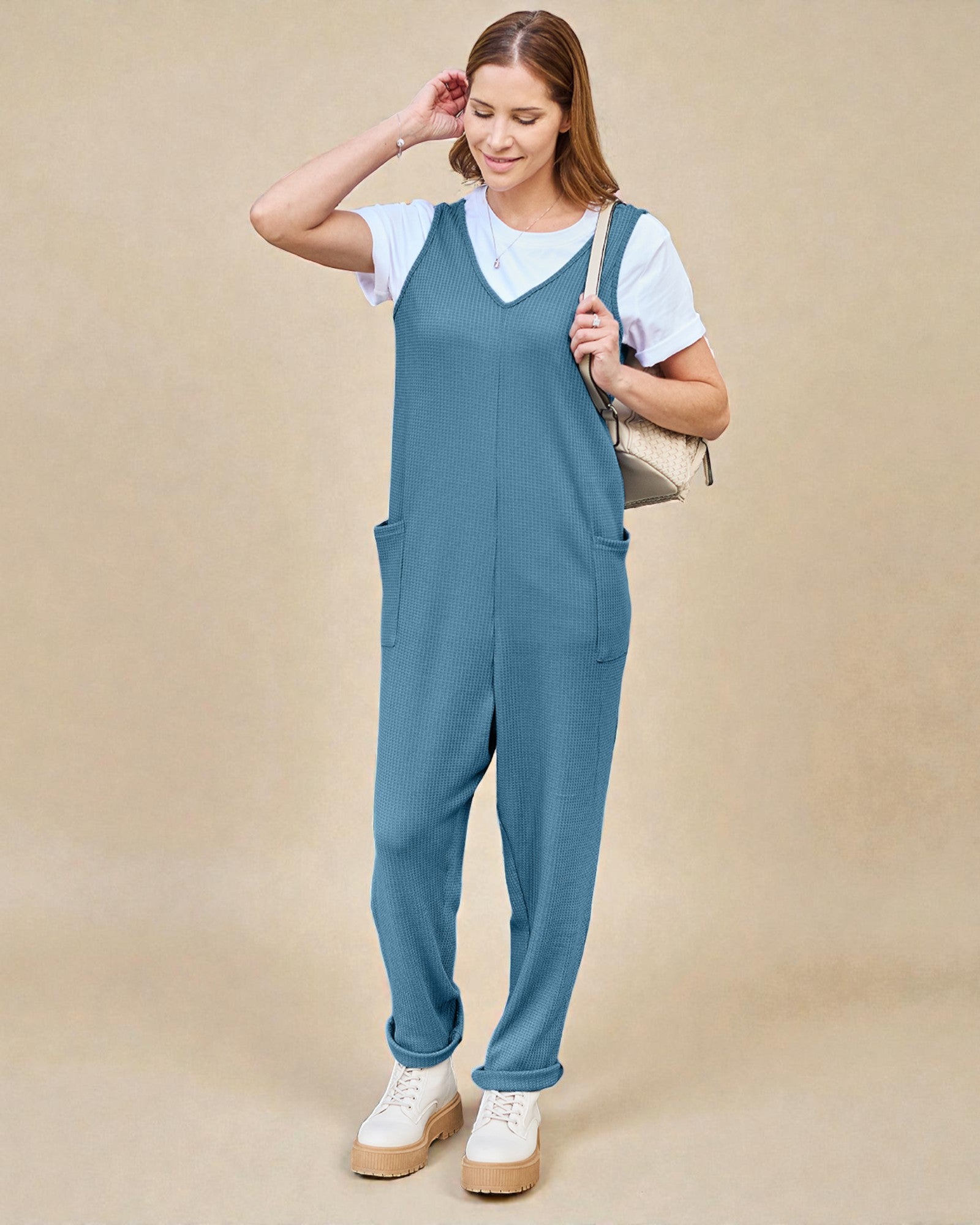 Woman wearing a blue jumpsuit over a white shirt on a beige background