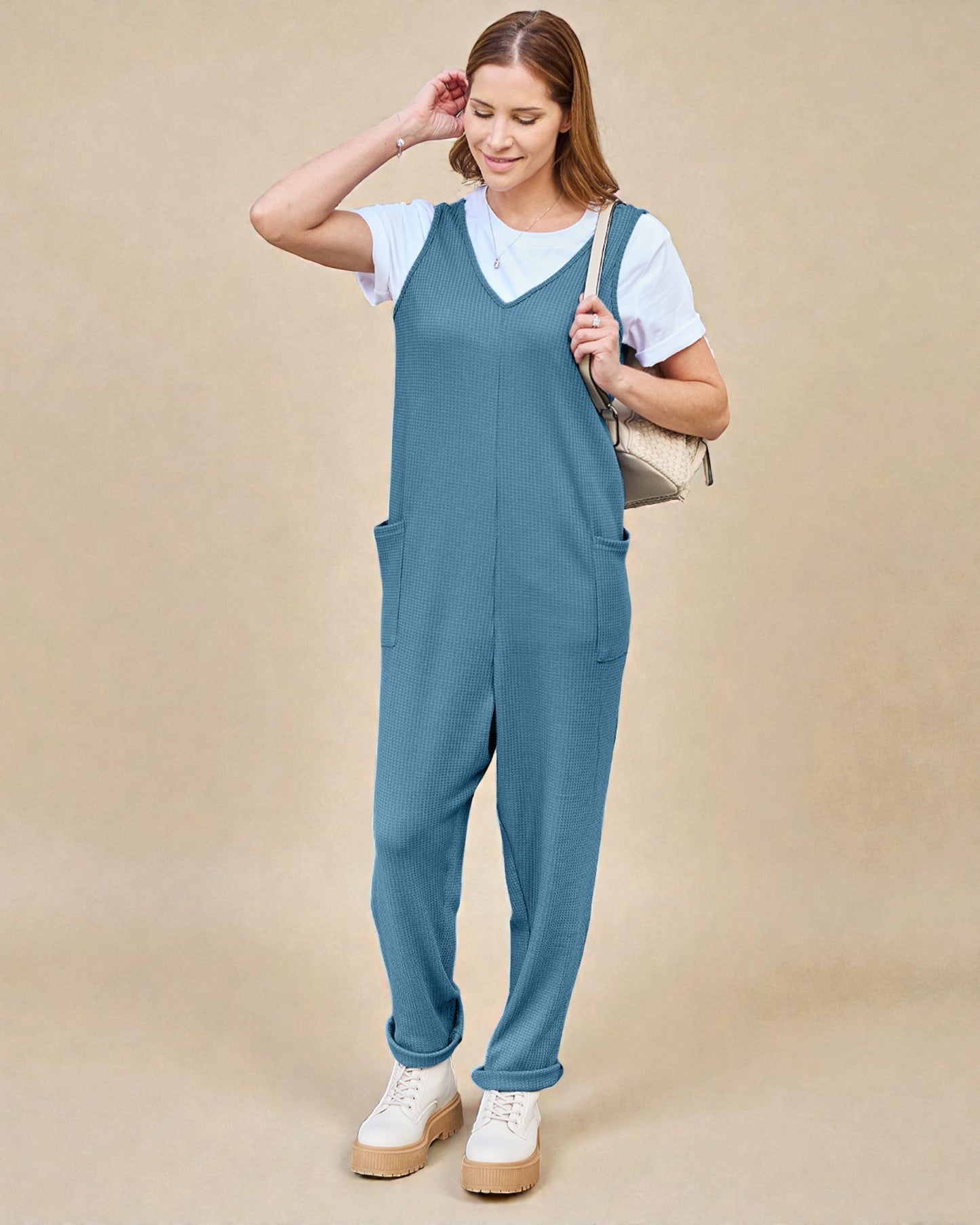 Woman wearing a blue jumpsuit over a white shirt on a beige background