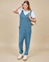 Woman wearing a blue jumpsuit over a white shirt on a beige background