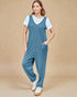 Woman wearing a blue jumpsuit over a white shirt on a beige background