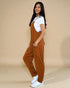 Woman wearing a brown jumpsuit over a white shirt on a beige background