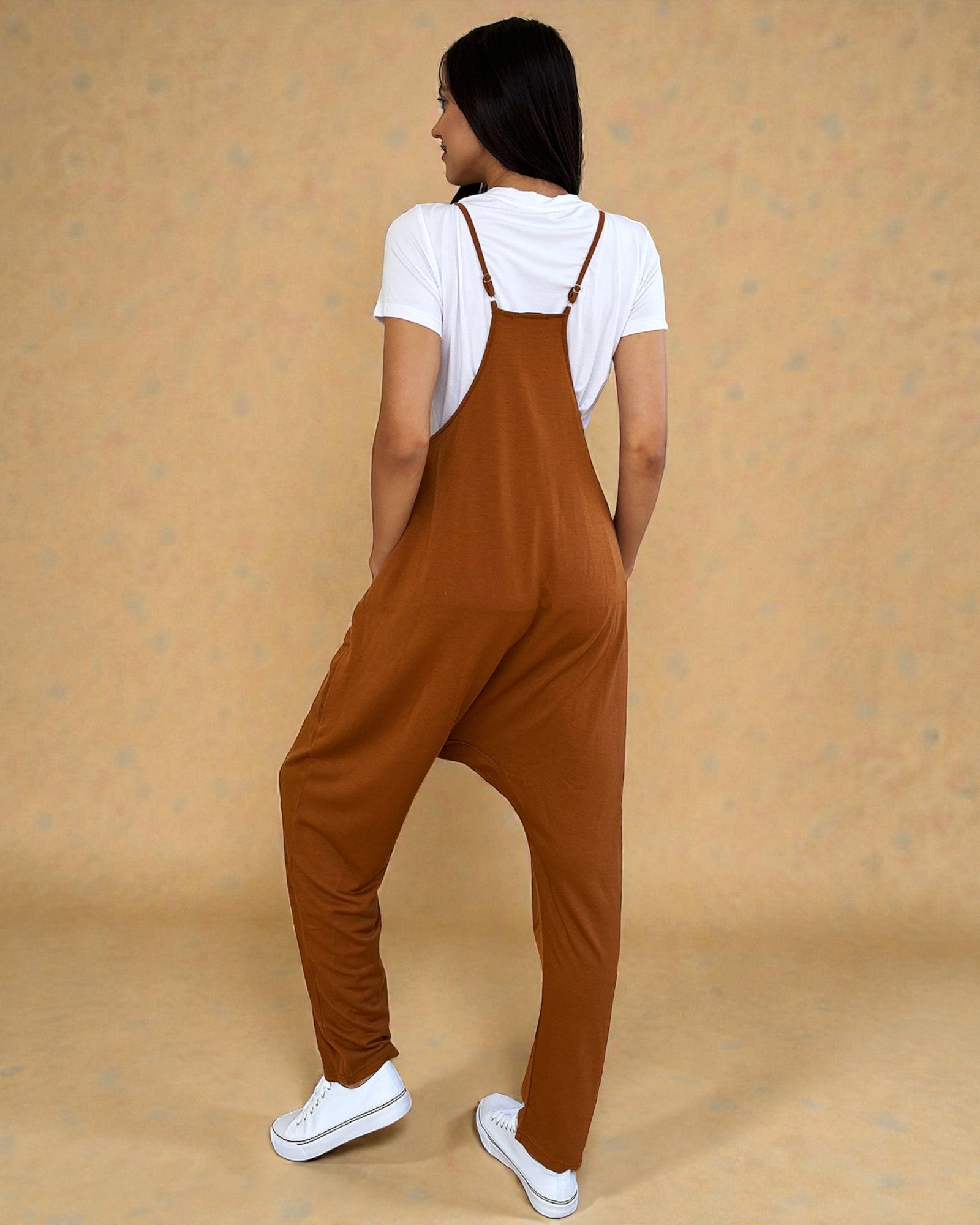 Person wearing brown overalls and white sneakers on a beige background