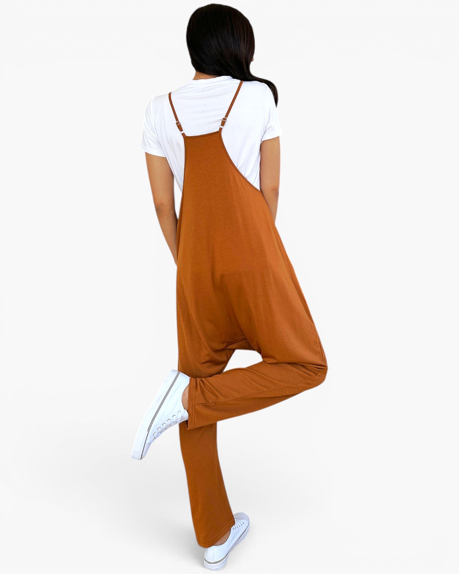 A woman shown from the back wearing a rust-orange overall jumpsuit over a white t-shirt and white sneakers, set against a plain white background.