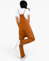 A woman shown from the back wearing a rust-orange overall jumpsuit over a white t-shirt and white sneakers, set against a plain white background.