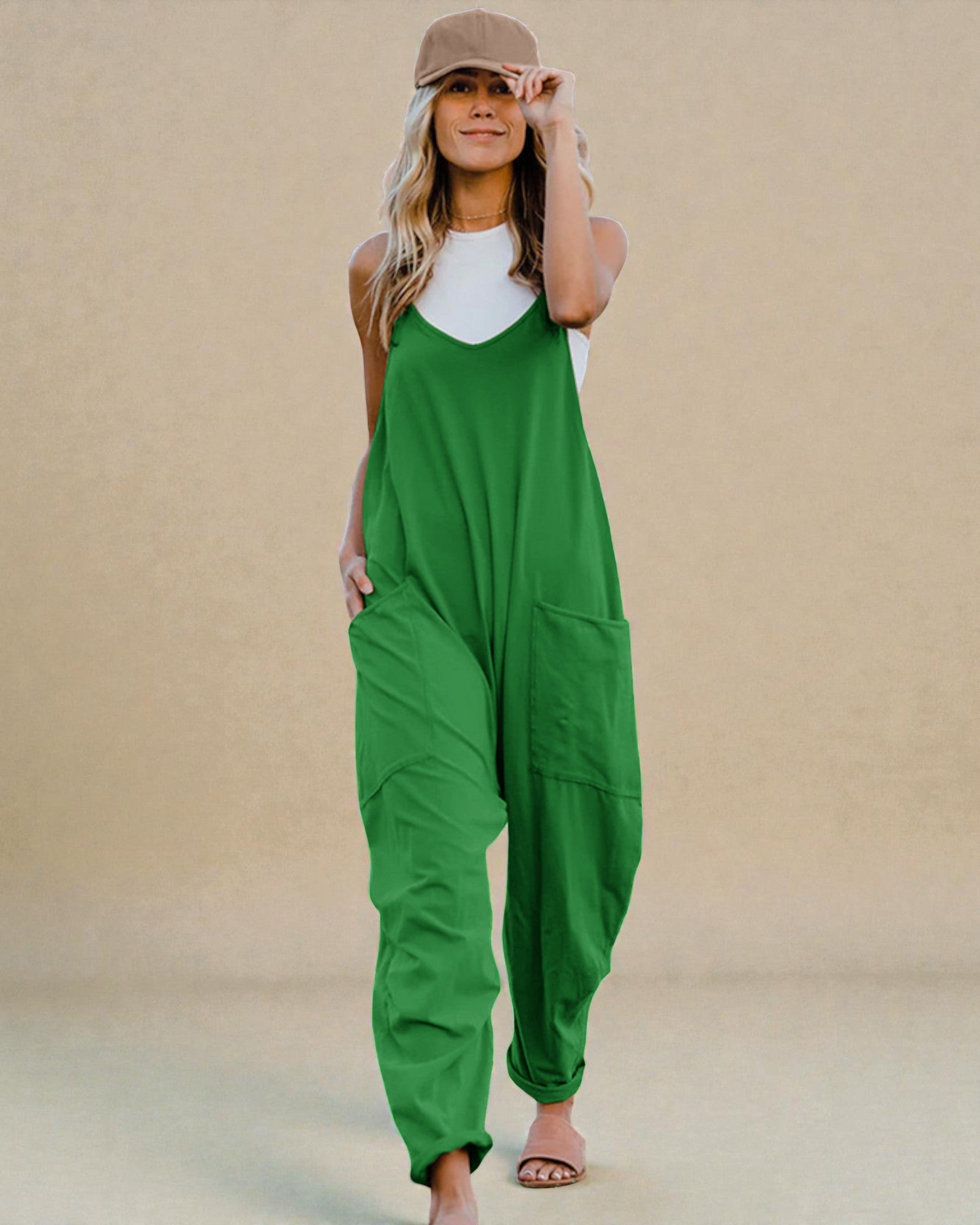 Woman wearing a green jumpsuit and beige cap against a beige background
