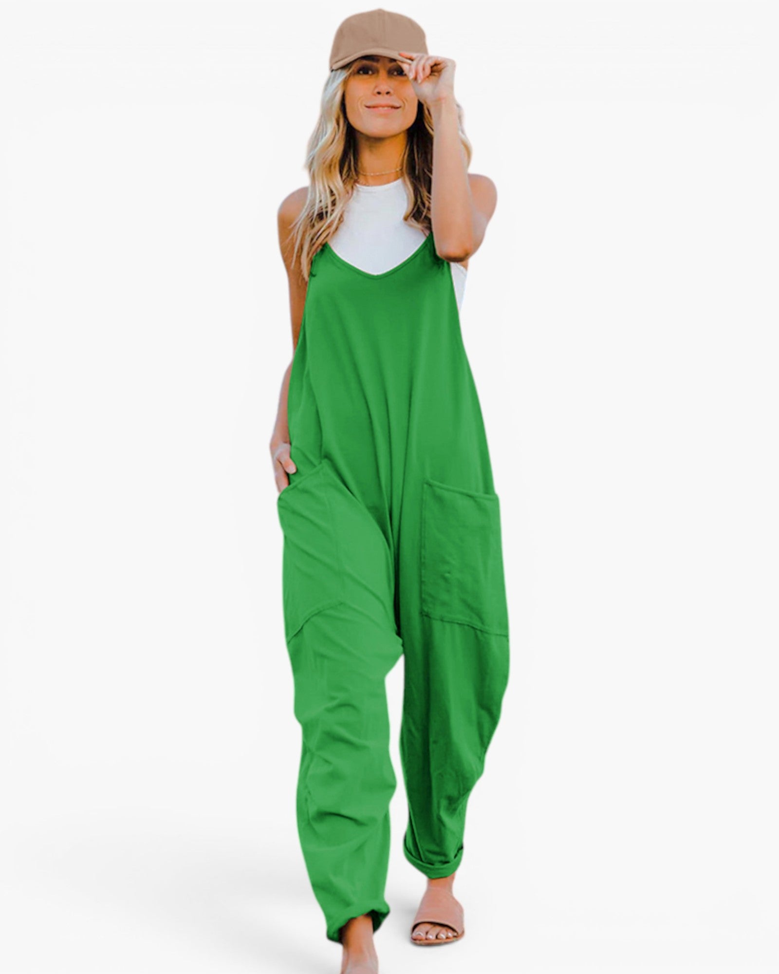 A woman modeling bright green wide-leg jumpsuit with a white tank top and beige baseball cap, standing against a plain white background.