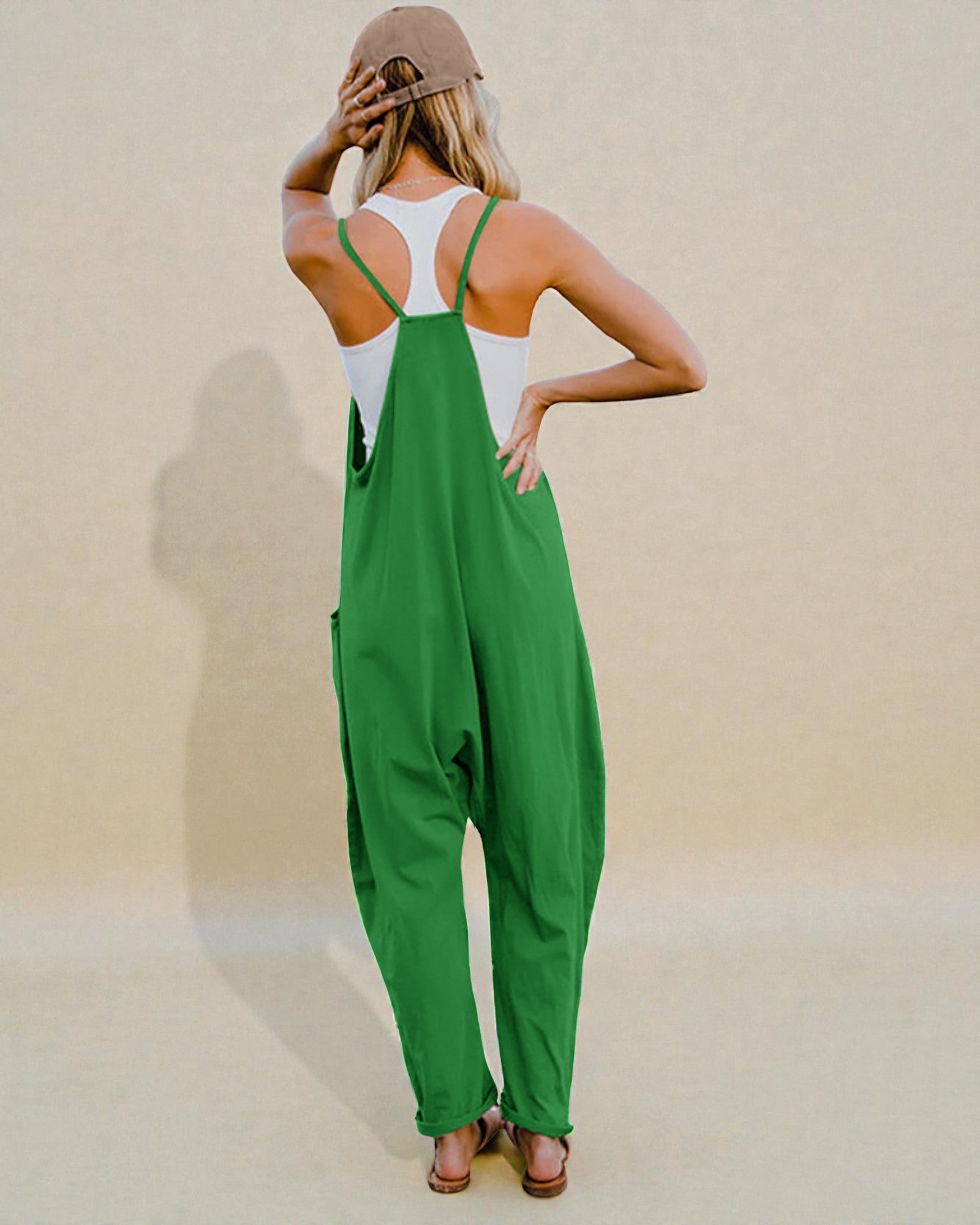Person wearing a green jumpsuit and white tank top with a beige cap on a plain background