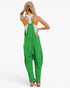 A woman shown from the back wearing bright green overall-style coveralls over a white tank top, with a beige hat and sandals, against a plain light background.