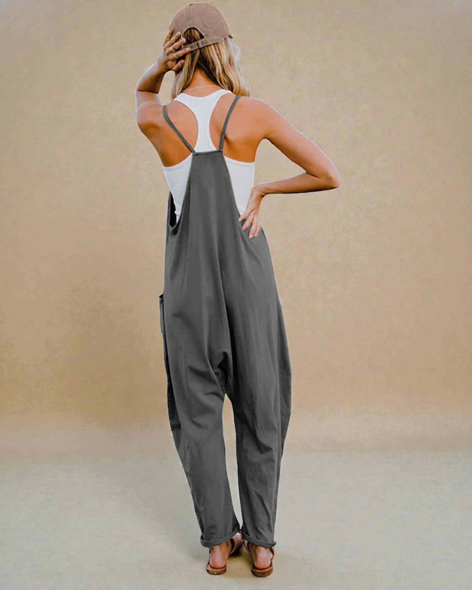 Woman wearing a gray jumpsuit and white tank top against a beige background