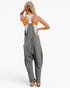 A woman shown from the back wearing a gray wide-leg jumpsuit over a white tank top, with a beige cap and brown sandals, against a plain white studio background.