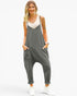 A woman modeling a dark gray sleeveless jumpsuit with a cream-colored inner top, styled with white sneakers against a plain white background.