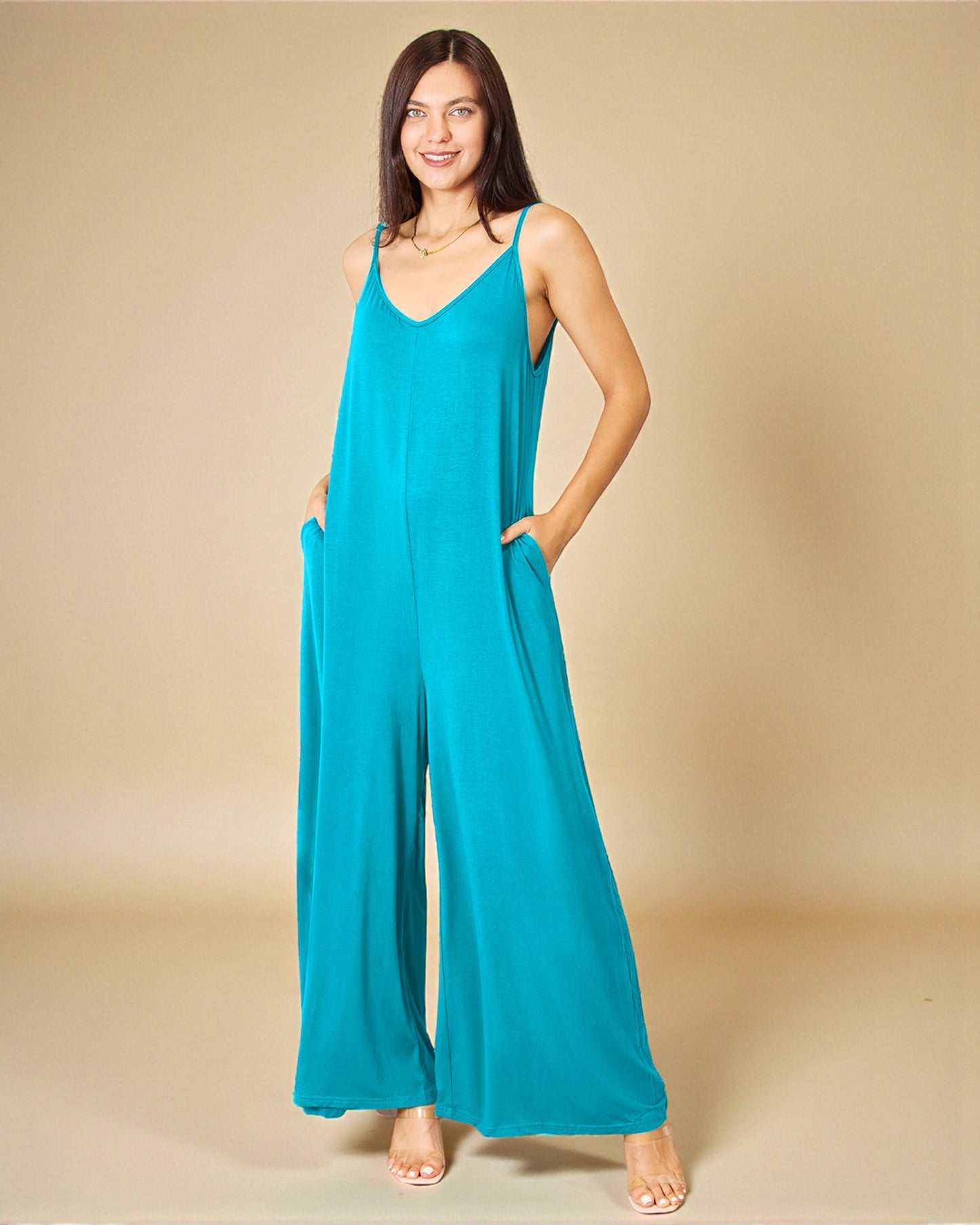 Woman wearing a teal jumpsuit against a beige background