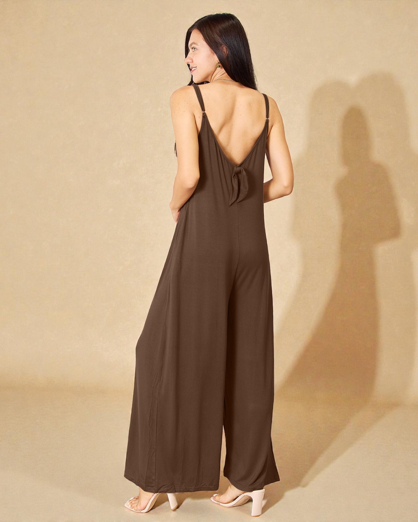 Woman wearing a brown jumpsuit with an open back against a beige background