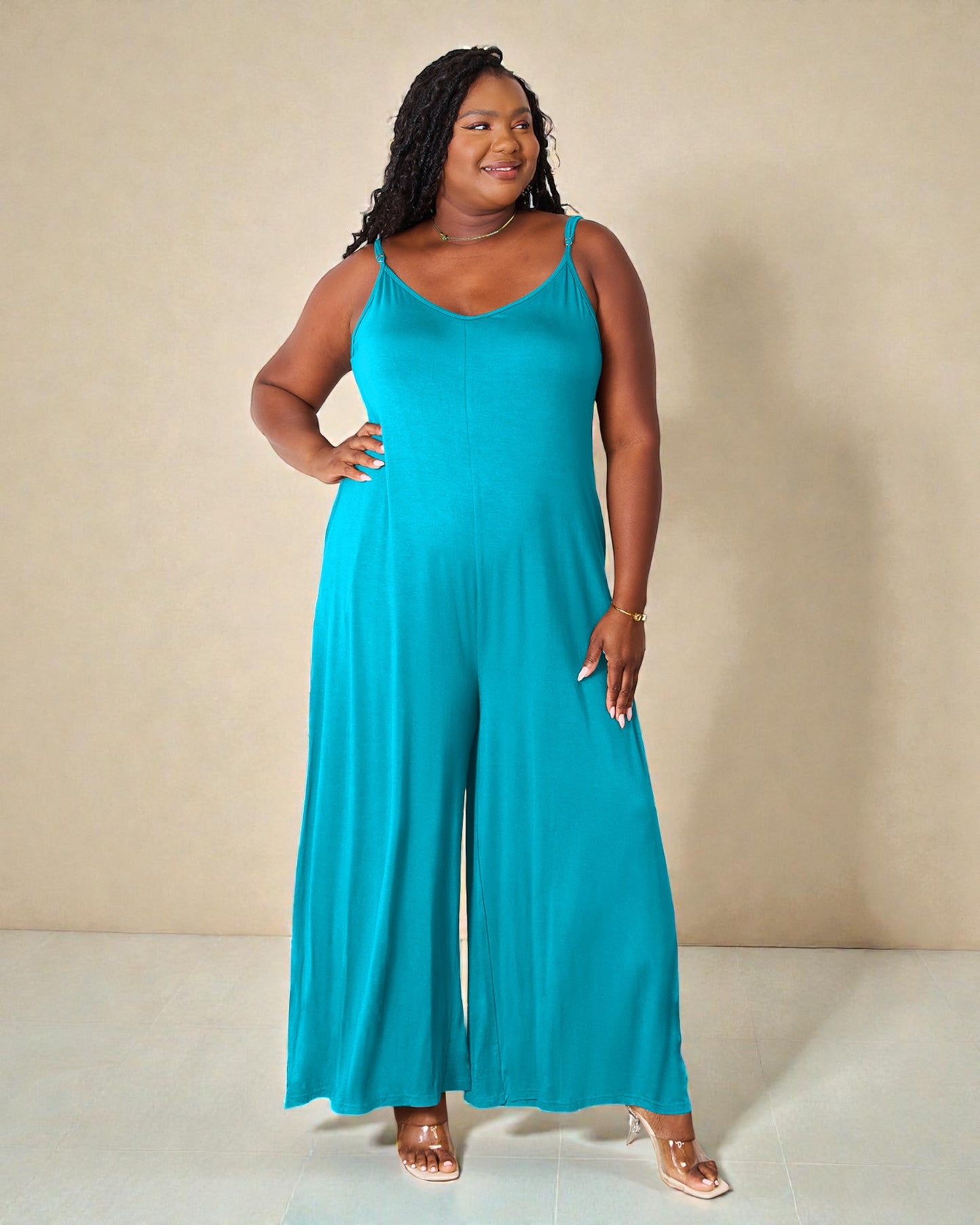 Woman wearing a teal jumpsuit against a beige background