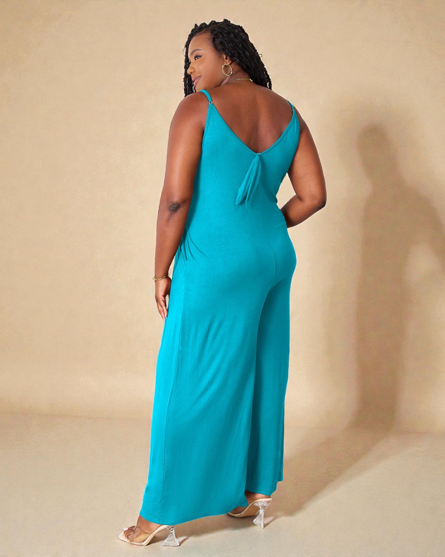 Woman wearing a teal jumpsuit against a beige background