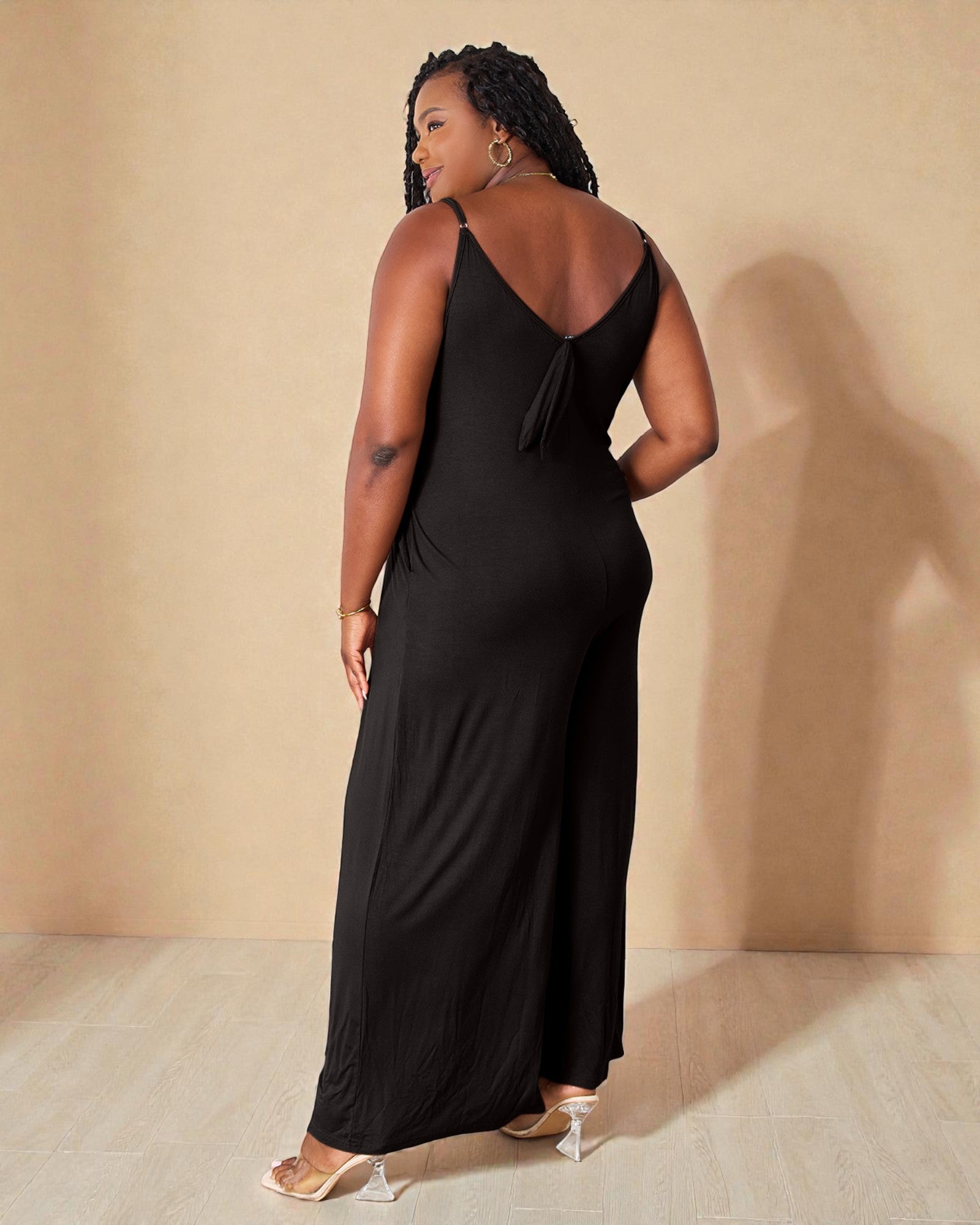 Woman wearing a black halter neck jumpsuit against a beige wall.