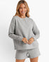 A woman modeling a light gray two-piece lounge set featuring a textured chevron-patterned long-sleeve top and matching shorts, set against a plain white studio background.
